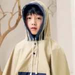 Poncho beige à capuche pour garçon, style moderne et protection pluie efficace. Coupe ample et finitions bleu marine pour un look propre.