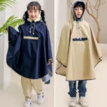 Poncho enfant bleu marine et poncho beige côte à côte. Deux modèles imperméables, capuche doublée et coupe large pour rester au sec avec style.