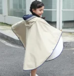 Poncho de pluie beige pour enfant, coupe ample et capuche bleu marine. Idéal pour la marche en extérieur, protection imperméable et look élégant.