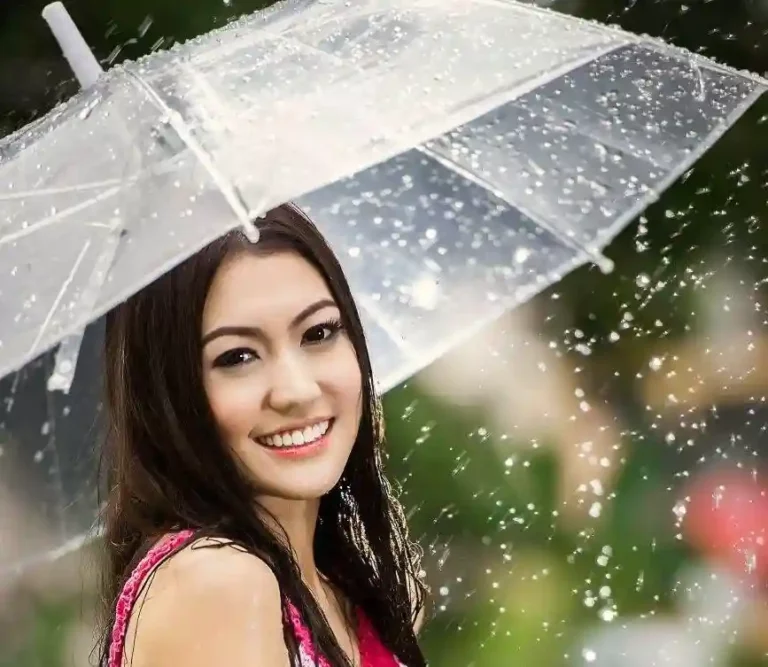 Portrait lumineux d’une femme sous la pluie, protégée par un parapluie transparent. Élégance naturelle.