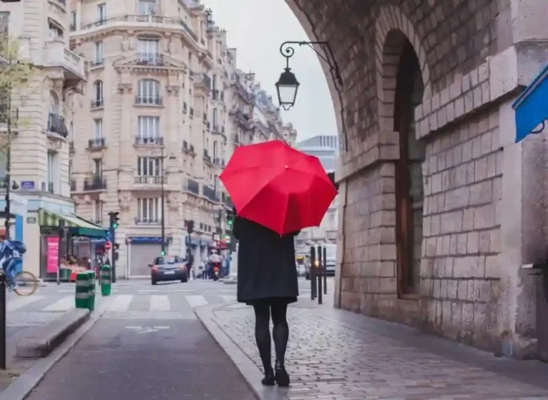 Ambiance parisienne : femme élégante avec parapluie rouge en pleine ville. Scène lifestyle stylée.
